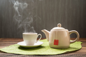 hot tea with steam and teapot on a table background. hot tea and teapot on leaf shape mat