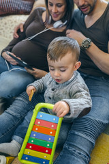 Pregnant woman and her husband looking at the tablet while their little son plays