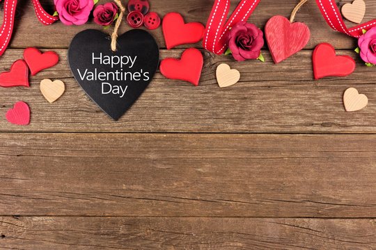 Happy Valentines Day message on a heart shaped chalkboard tag with ribbon and hearts border against a rustic wood background