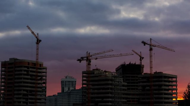 Zoom in timelapse of construction site with cranes working on building complex with blurred natural background sunset pastel. Construction crews work on high ground heavy industry and safety concept. 
