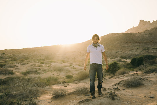 young man in used cowboy look walking through the desert at sunset