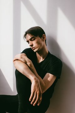 Vertical portrait of young handsome brunet in contrast lightning  and his shadow on white wall