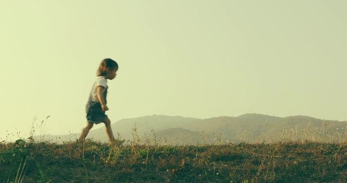Happy child running outdoors. Little girl playing around the park on beautiful morning. Healthy preschool children summer activity. Kids playing outside. Little girl running on meadow with sunset.