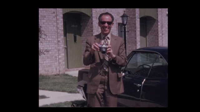 1970 Man with camera takes picture playing to camera