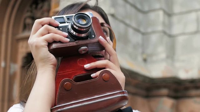 Closeup slow motion portrait of smiling young girl posing with vintage film camera on street