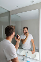 Man shaving using electric shaver trimming his beard in home bathroom- morning grooming routine...