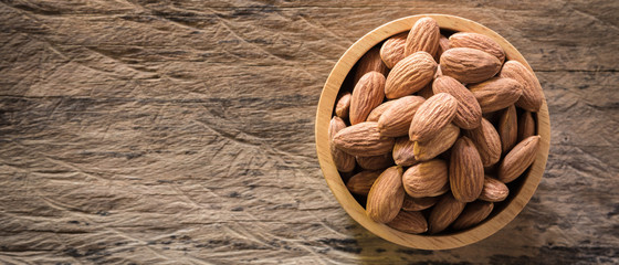 Almonds in brown bowl on textured wooden background.