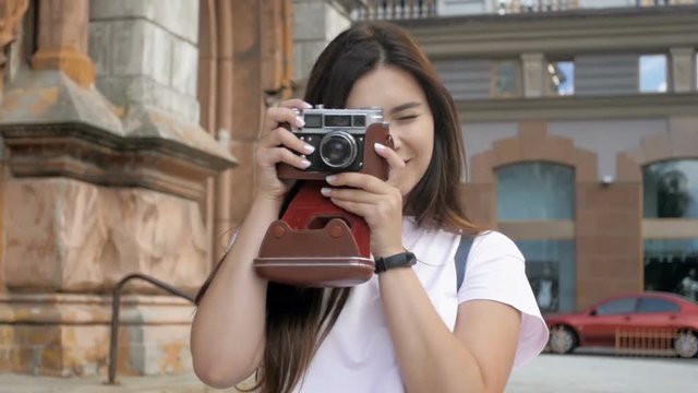 Slow motion video of smiling brunette tourist girl walking and making photos with old film camera