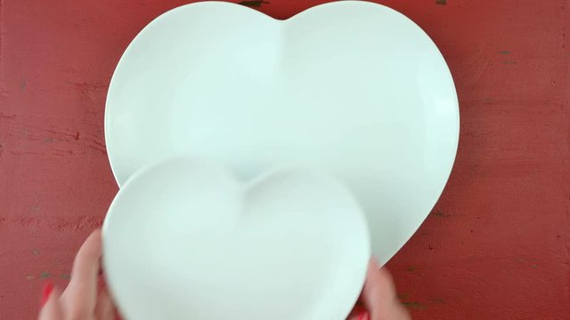 Valentine romantice place setting with heart shaped plates and red rose, time lapse overhead on red rustic wood table.