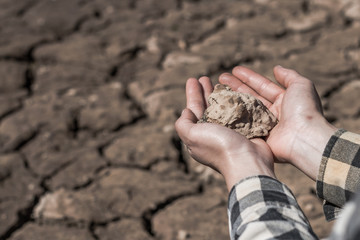 Hand woman holds a dry clay dirt with despair on dry soil background.