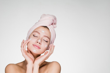 a cute young girl with a towel on her head puts a nourishing cream on her face, her eyes are closed, she enjoys - 187568839