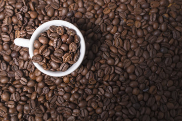 Brown coffee beans background with a full white espresso coffee cup