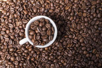 White coffee cup with roast coffee beans on a brown coffee grains background