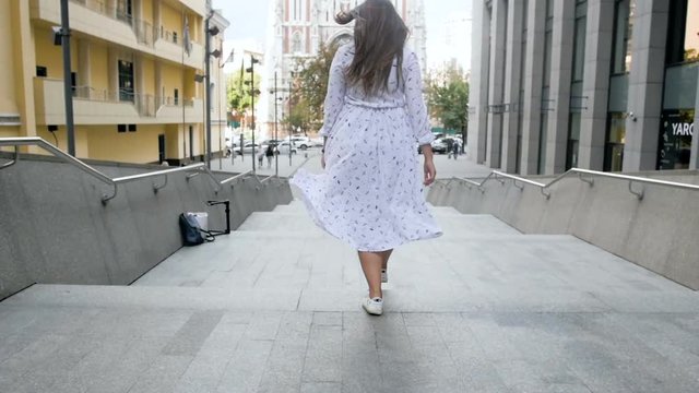 Slow motion footage of cheerful girl with long hair walking down the stone stairs on street