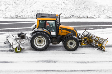 Large snow plowing tractor machine at work on the road during a snow storm in winter.