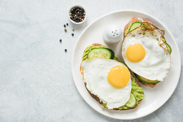 Healthy breakfast toasts with fried egg, avocado and cucumber on white plate. Top view and copy space for text. Concept of healthy eating, healthy lifestyle and dieting