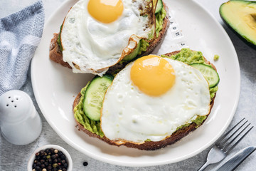 Healthy breakfast toasts with fried egg, avocado and cucumber on white plate. Closeup view. Concept of healthy eating, healthy lifestyle and dieting