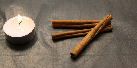 cinnamon sticks, lighted candle on a black background