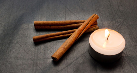 cinnamon sticks, lighted candle on a black background