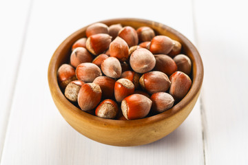 Hazelnut nuts in a wooden bowl on a white wooden table. Superfood.