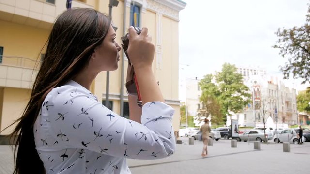 Closeup slow motion footage of beautiful brunette girl with long hair using vintage manual camera on street
