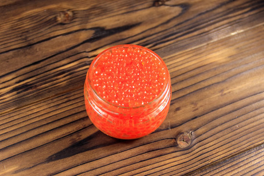 Red caviar in glass jar on wooden table