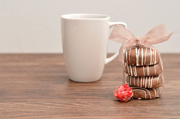 A stack of chocolate covered biscuits tied with a pink ribbon, an artificial rose and a  white mug
