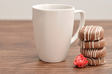 A stack of chocolate covered biscuits with an artificial rose and a  white mug