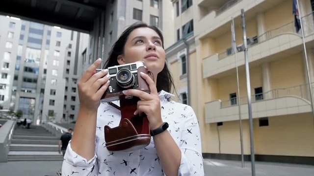 Slow motion video of happy young woman with long hair making photographs of modern building with old manual camera