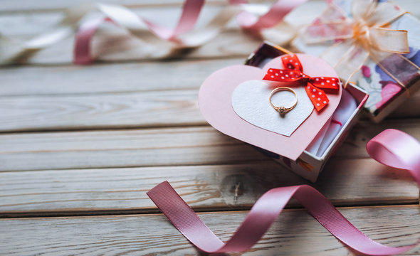 A gift for Valentine's Day. A wedding ring on a gift box with ribbons and hearts on a wooden background. Festive decor. View from above. Marriage proposal.