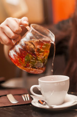 The girl pours hot fruit tea in a white mug.