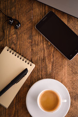  Laptop (notebook) mobile phone (smartphone) and notepad with pen on old wooden table. Work place modern.Cup of coffee