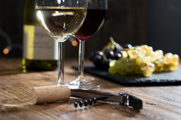 two glass of red and white wine on wooden restaurant table with a corkscrew and grape