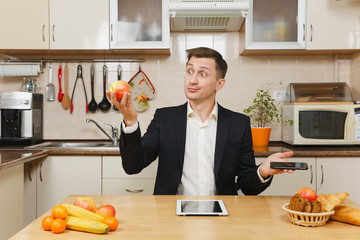 Handsome young business man in suit, shirt, having breakfast, sitting at table with tablet, talking...