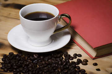 White cup with a drink, fried coffee beans and a red book