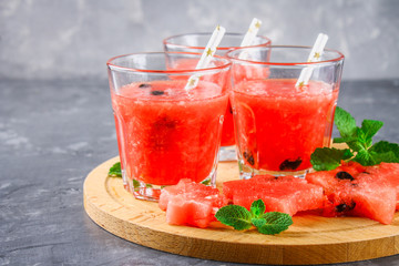Watermelon smoothies in glasses with mint leaves on a gray dark concrete background.
