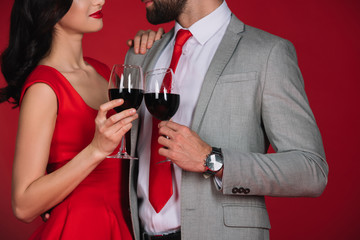 cropped image of couple clinking with glasses of wine and looking at each other isolated on red