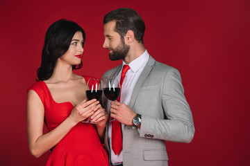 couple clinking with glasses of wine and looking at each other isolated on red