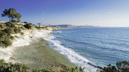 The coastline and landmark big white chalk rock at Governor's beach, Limassol, Cyprus. Steep stone cliffs and deep blue sea waves crushing in coves and dark sand next to Vasilikos power station.