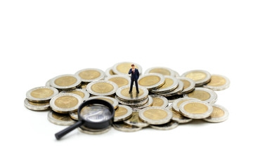 Miniature people : Businessman standing on the coins stack with Magnifying glass.