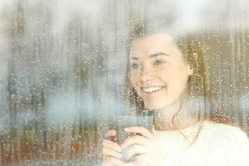 Positive teen looking through a window in a rainy day