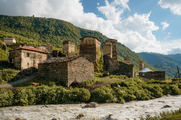 Fototapeta premium old weathered buildings against small river stream against hills, Ushguli, svaneti, georgia
