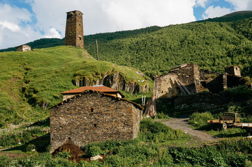 Fototapeta na wymiar view of grassy field with old weathered rural buildings and hills on background, Ushguli, svaneti, georgia