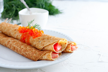 Homemade pancakes with red caviar on a white table with fresh herbs, horizontal, copy space