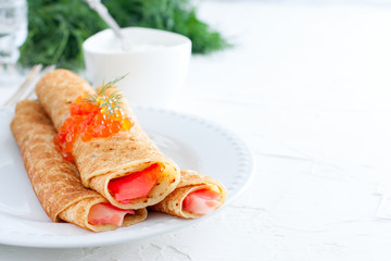 Homemade pancakes with red caviar on a white table with fresh herbs, horizontal, copy space