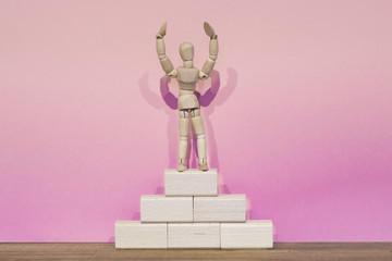 Small wooden figure on the winner's podium, pink background