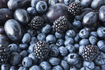Blue and black food. Background of fruits and berries. Fresh blackberries, blueberries, plums and grapes. Top view. Blue-black fruits.
