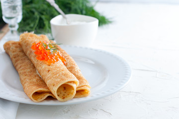 Homemade pancakes with red caviar on a white table with fresh herbs, horizontal, copy space