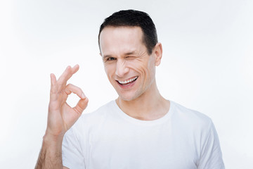 OK sign. Delighted happy handsome man smiling and winking while looking at you