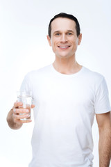 Healthy drink. Joyful nice positive man holding a glass of water and smiling while standing against white background